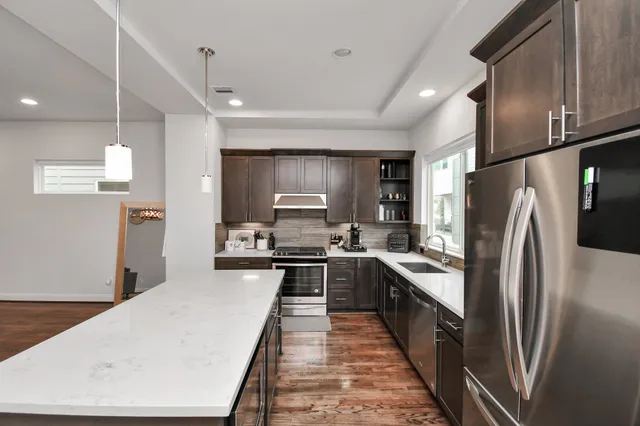 a large kitchen with stainless steel appliances a refrigerator a sink dishwasher a stove and white cabinets with wooden floor