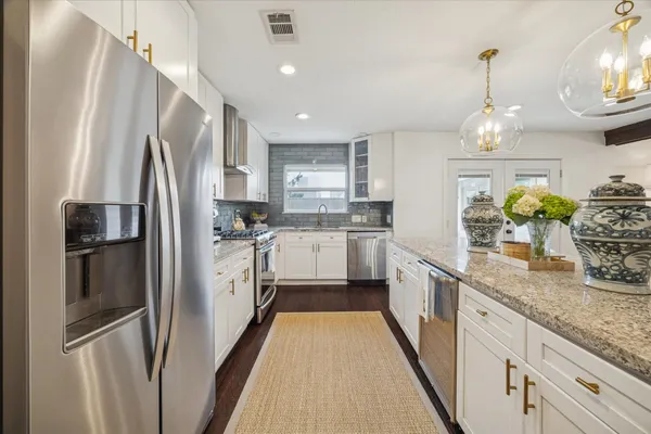 a kitchen with stainless steel appliances granite countertop a refrigerator a sink dishwasher a stove and a dining table with wooden floor