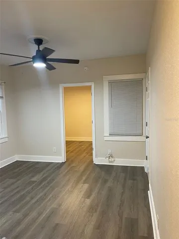 a view of an empty room with wooden floor and a ceiling fan