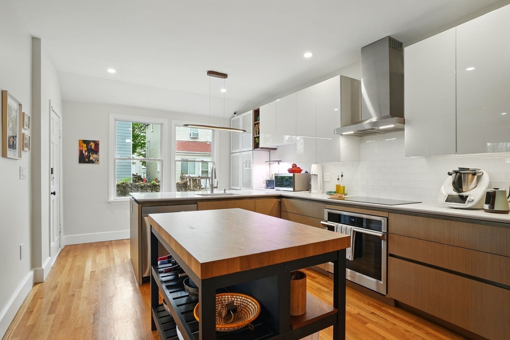 25 Bowdoin Street Somerville, MA 02143 - Photo 10 of 28 a kitchen with stainless steel appliances a table chairs in it and wooden floors