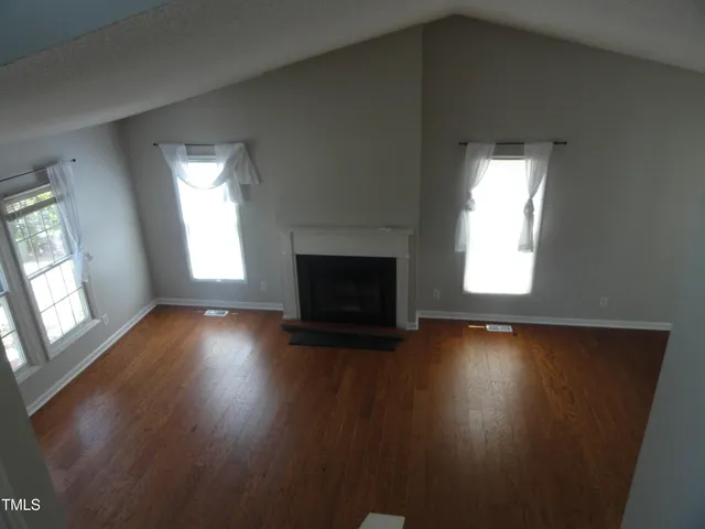 an empty room with wooden floor fireplace and windows