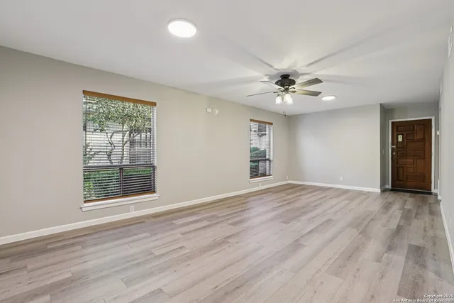 an empty room with wooden floor chandelier fan and windows