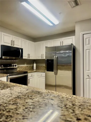a kitchen with stainless steel appliances kitchen island granite countertop a refrigerator and a stove top oven