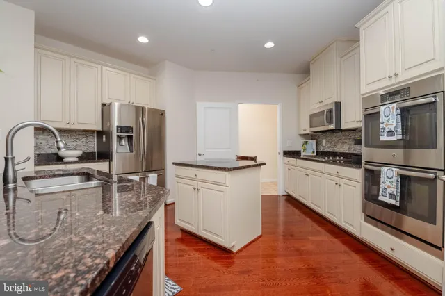 a kitchen with stainless steel appliances granite countertop a refrigerator a stove a sink and white cabinets