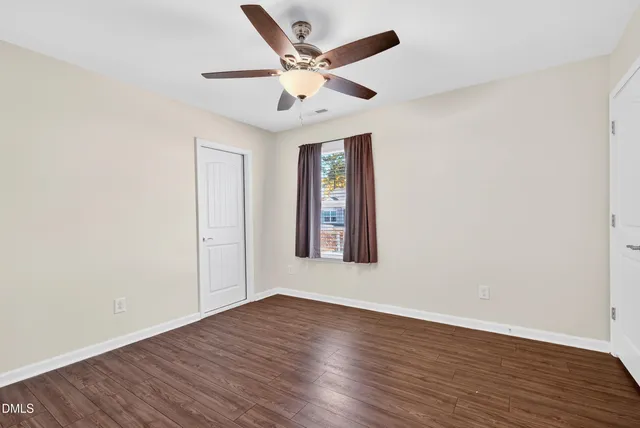 an empty room with wooden floor ceiling fan and windows