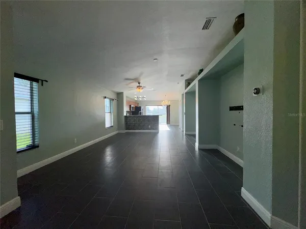 an empty room with wooden floor kitchen view and windows