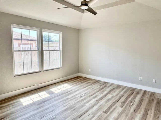 an empty room with wooden floor fan and windows