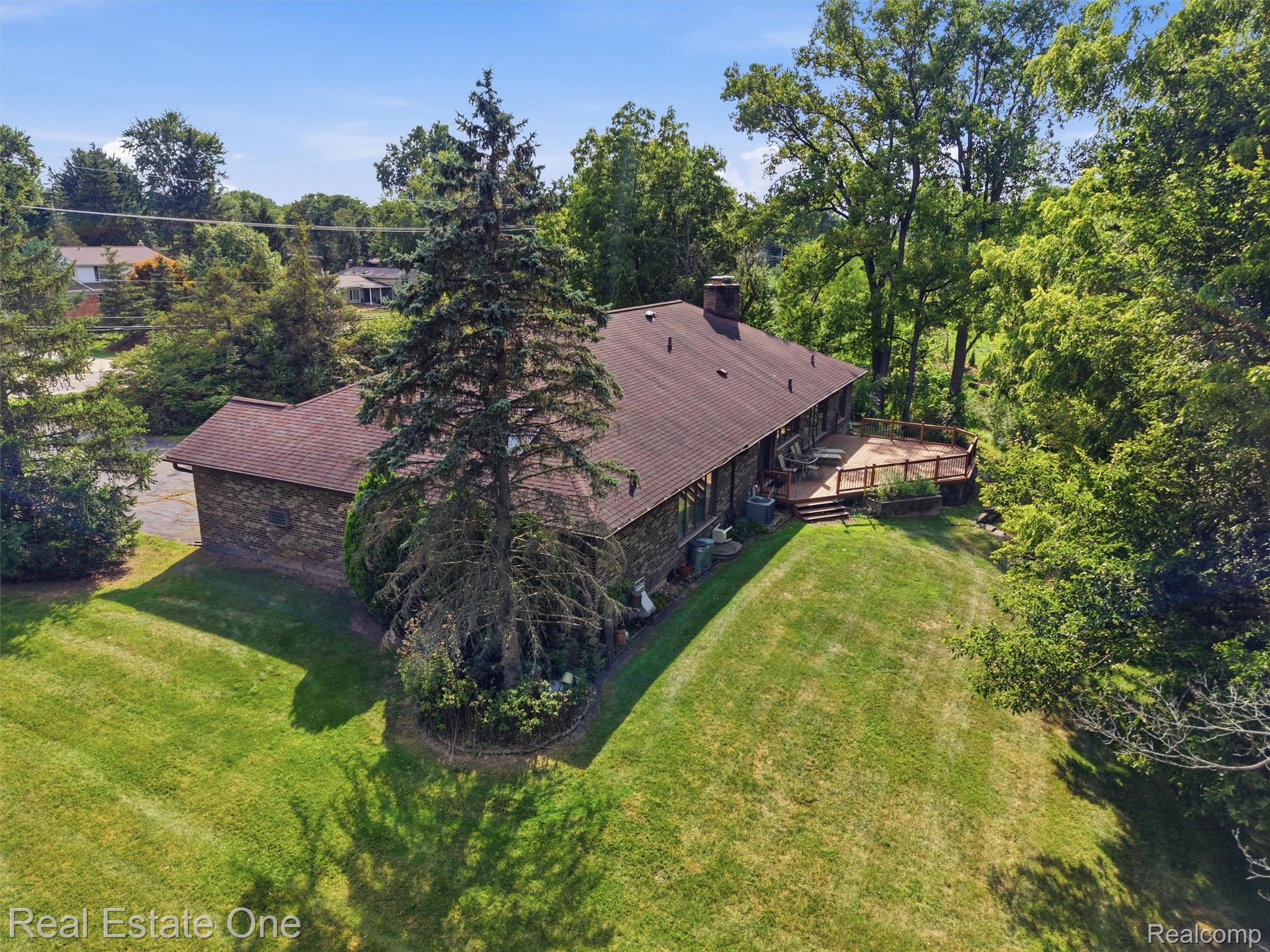 2626 West Wattles Road Troy, MI 48098 - Photo 61 of 65 Expansive green lawn surrounding a residence with a large wooden deck, mature trees, and a dark shingled roof