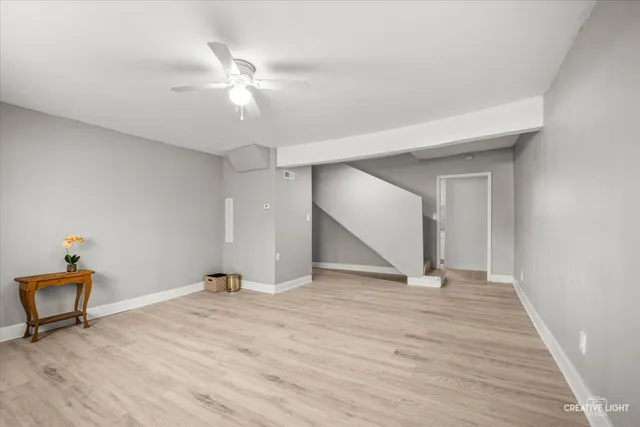 a view of an empty room with wooden floor and a ceiling fan