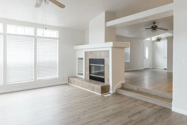 a view of a livingroom with a fireplace a chandelier fan and wooden floor