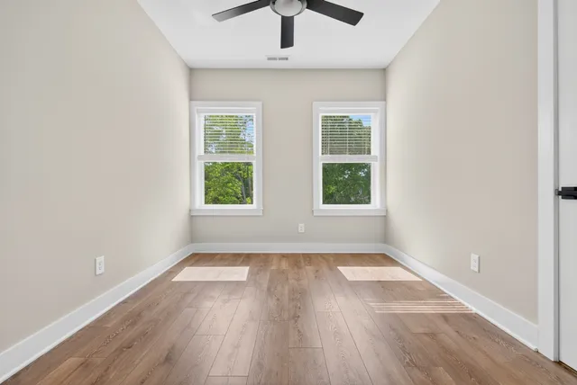 an empty room with wooden floor chandelier fan and windows