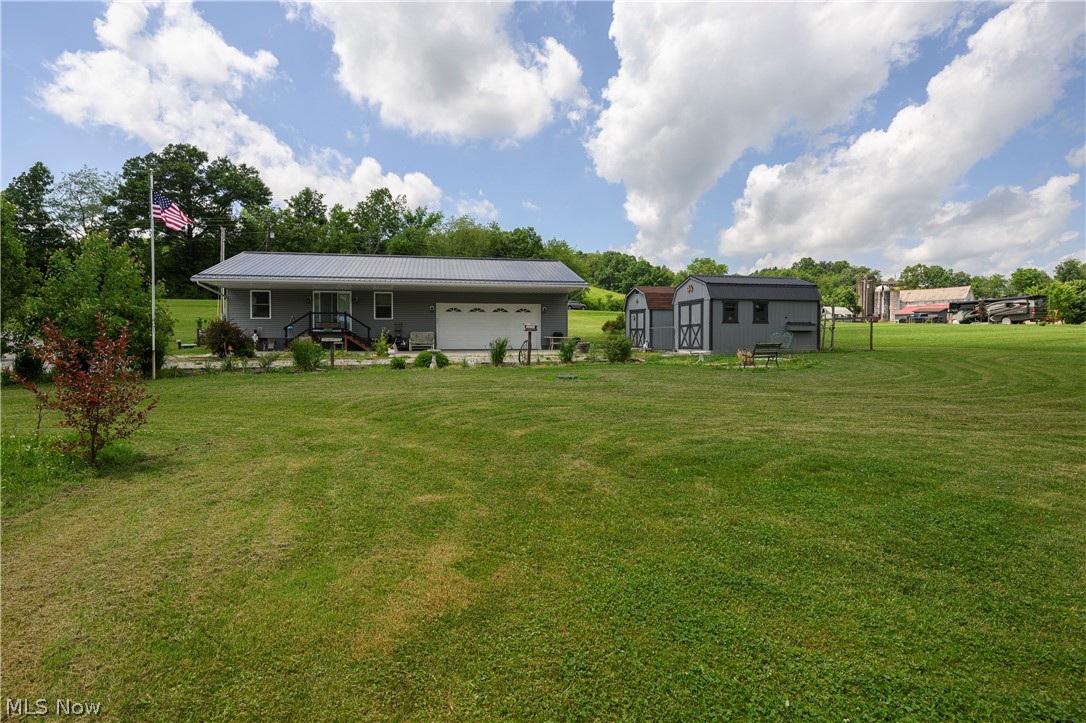 9427 Stonecreek Road Southwest Newcomerstown, OH 43832 - Photo 3 of 29 Expansive green lawn with a gray siding residence featuring a metal roof and an attached garage with a white door