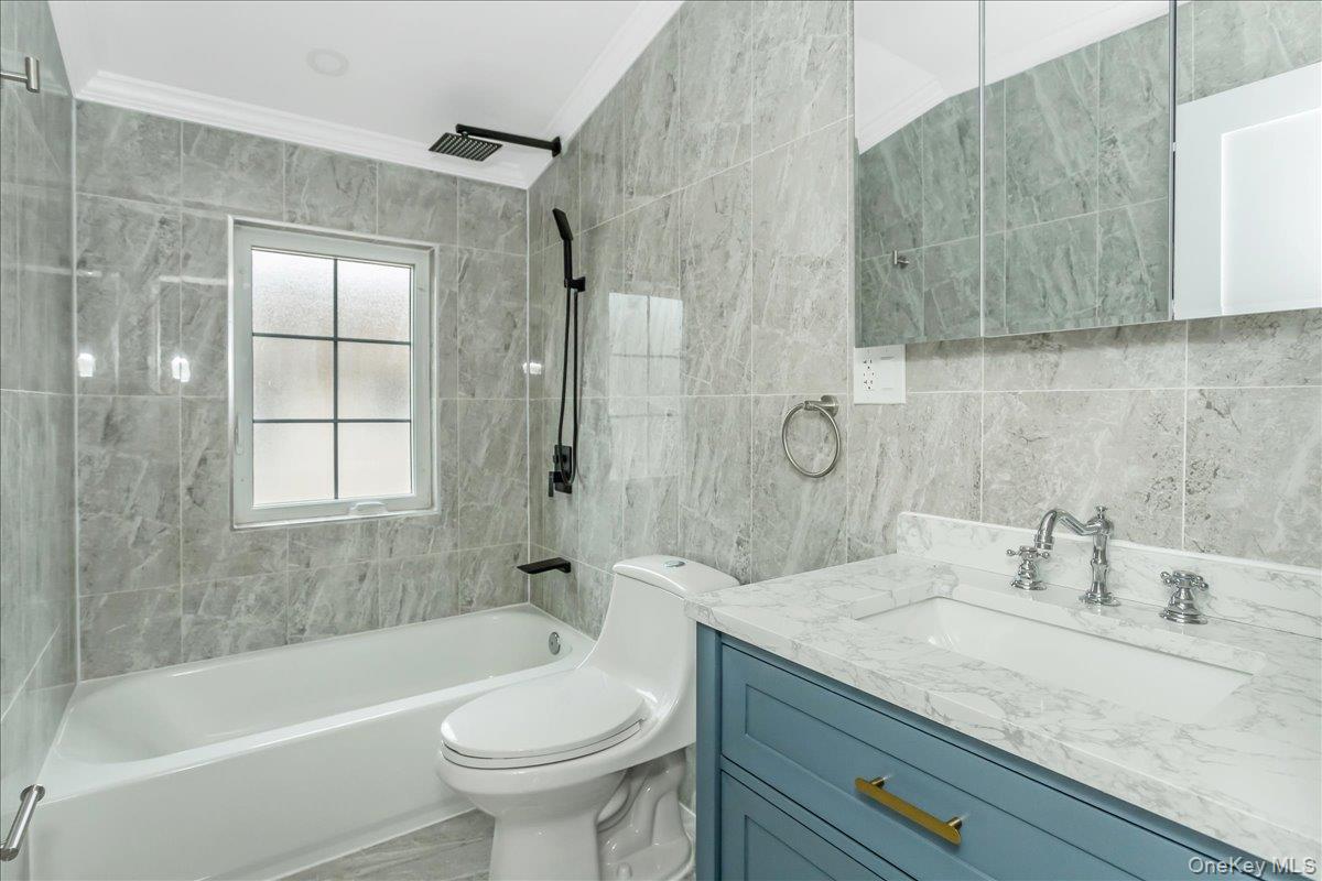 243-36 Caney Road Queens, NY 11422 - Photo 26 of 30 Bathroom featuring tile walls, shower / bath combination, vanity, and ornamental molding