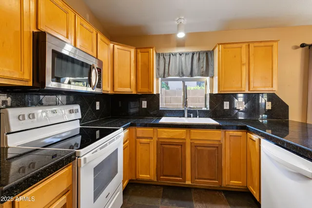 a kitchen with granite countertop a sink cabinets stainless steel appliances and a window
