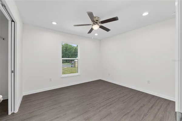 an empty room with wooden floor window and ceiling fan