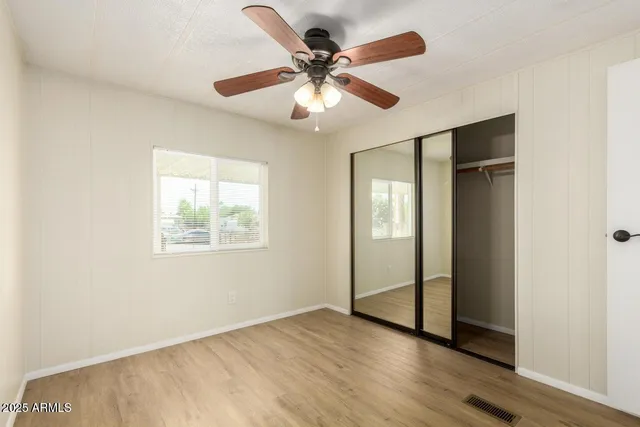 a view of an empty room with wooden floor and a ceiling fan