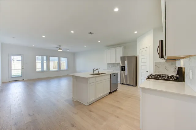 a large kitchen with stainless steel appliances a large counter top a stove a sink a refrigerator and a window