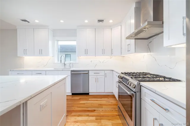 a kitchen with granite countertop a sink stove a refrigerator and white cabinets with wooden floor