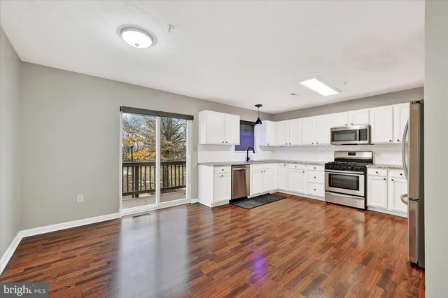 a kitchen with stainless steel appliances granite countertop a stove top oven a sink and white cabinets with wooden floor