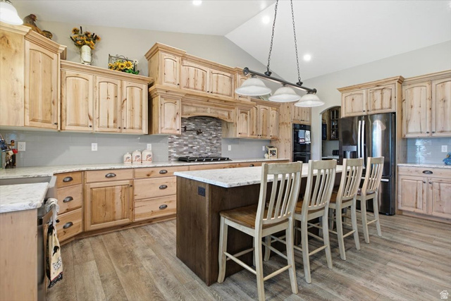 3123 East Riverdale Road Preston, ID 83263 - Photo 9 of 52 Kitchen featuring a central island with seating, natural wood cabinetry, light-toned countertops, and wood-finish flooring. Lower cabinets have pull out drawers.