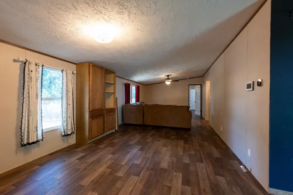 an empty room with wooden floor chandelier fan and windows