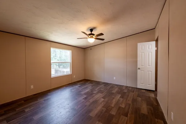 an empty room with wooden floor fan and windows