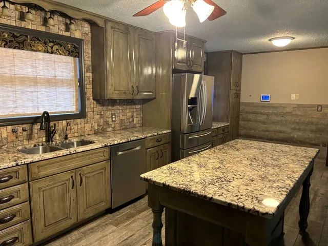 a kitchen with kitchen island granite countertop wooden cabinets a refrigerator and a sink