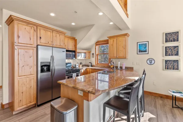 a kitchen with stainless steel appliances granite countertop a refrigerator a stove a sink a dining table and chairs with wooden floor