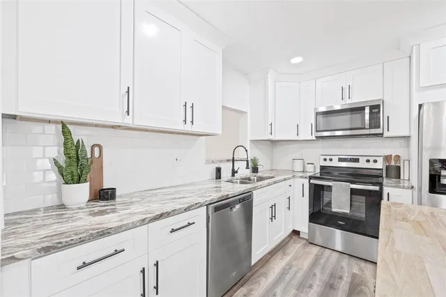 a kitchen with stainless steel appliances granite countertop a sink a stove top oven and white cabinets