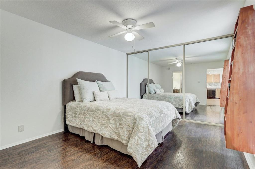 3115 Helms Street, Unit 204 Austin, TX 78705 - Photo 4 of 13 Rich hardwood floors complement this cozy bedroom, featuring mirrored closet doors and a ceiling fan.