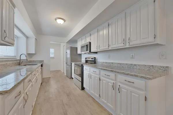 a kitchen with granite countertop a sink dishwasher stove and cabinets with wooden floor
