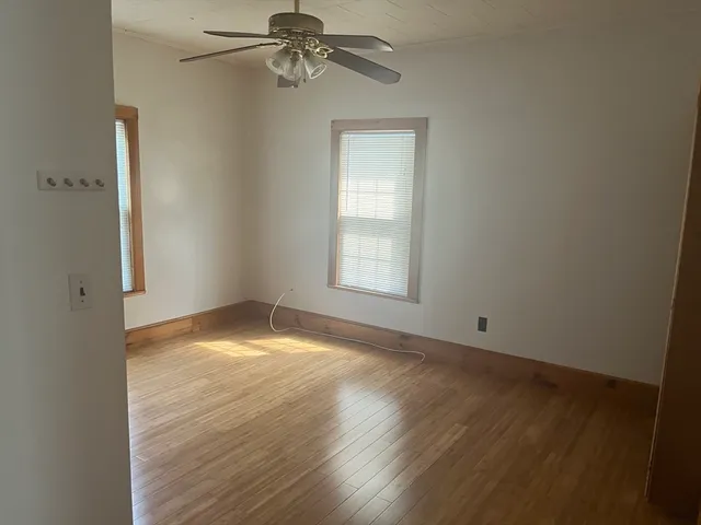 an empty room with wooden floor fan and windows