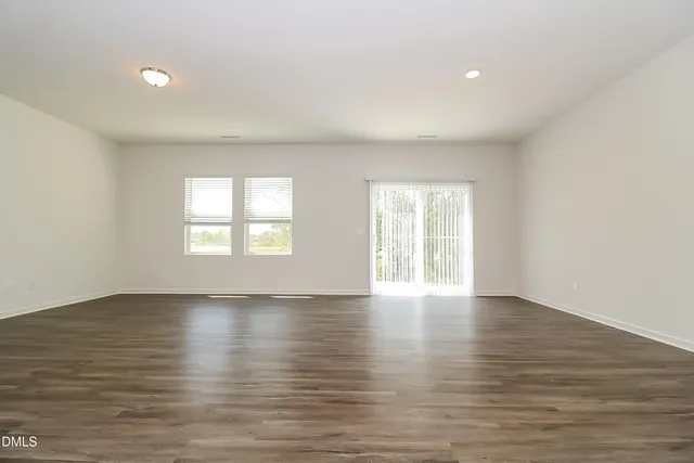 a view of an empty room with wooden floor and window