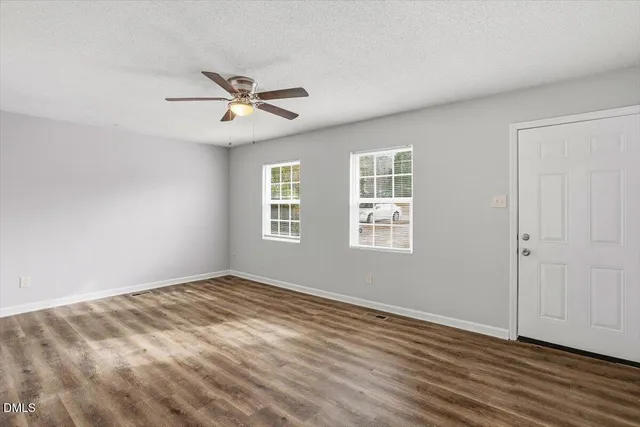 an empty room with wooden floor ceiling fan and windows