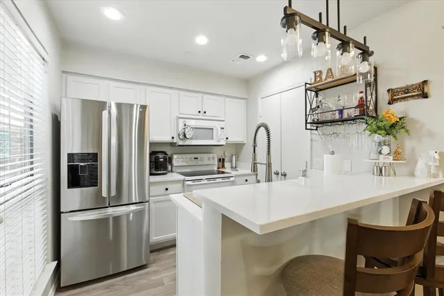 a kitchen with stainless steel appliances a sink a stove a refrigerator cabinets and chairs