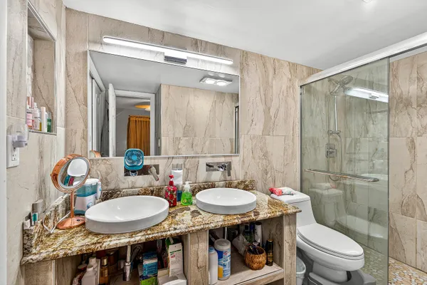 a bathroom with a granite countertop sink a toilet a mirror and shower