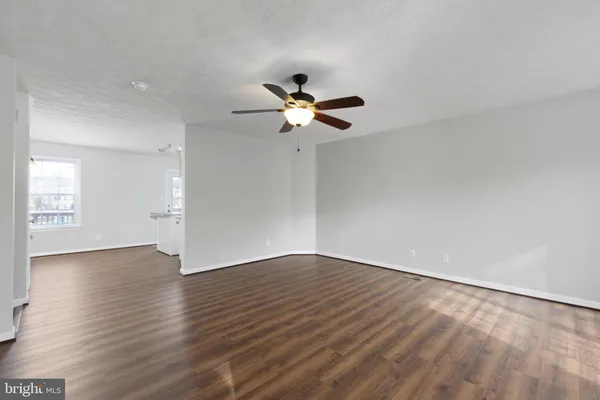 a view of an empty room with wooden floor and a ceiling fan