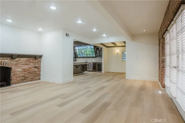 an empty room with wooden floor and kitchen view