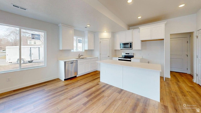 783 Pheasantbrook Drive, Unit 2A Centerville, UT 84014 - Photo 9 of 41 Modern kitchen featuring a central island, white cabinetry, stainless steel appliances, and wood-finish flooring