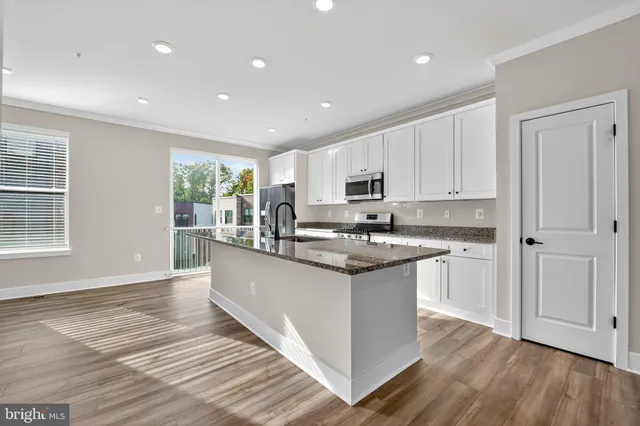 a kitchen with stainless steel appliances granite countertop a stove top oven a sink and white cabinets with wooden floor