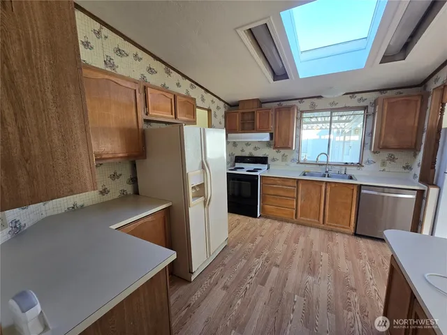 a kitchen with stainless steel appliances granite countertop a refrigerator a sink dishwasher a stove and white countertops with wooden floor