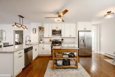 a kitchen with stainless steel appliances granite countertop a refrigerator a stove top oven a sink dishwasher and white cabinets with wooden floor