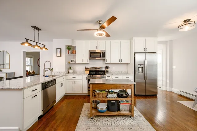 a kitchen with stainless steel appliances granite countertop a refrigerator a stove top oven a sink dishwasher and white cabinets with wooden floor
