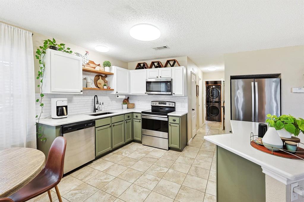 1016 Ridgetop Drive Justin, TX 76247 - Photo 11 of 40 Kitchen featuring green cabinetry, stacked washer / dryer, stainless steel appliances, backsplash, and a textured ceiling