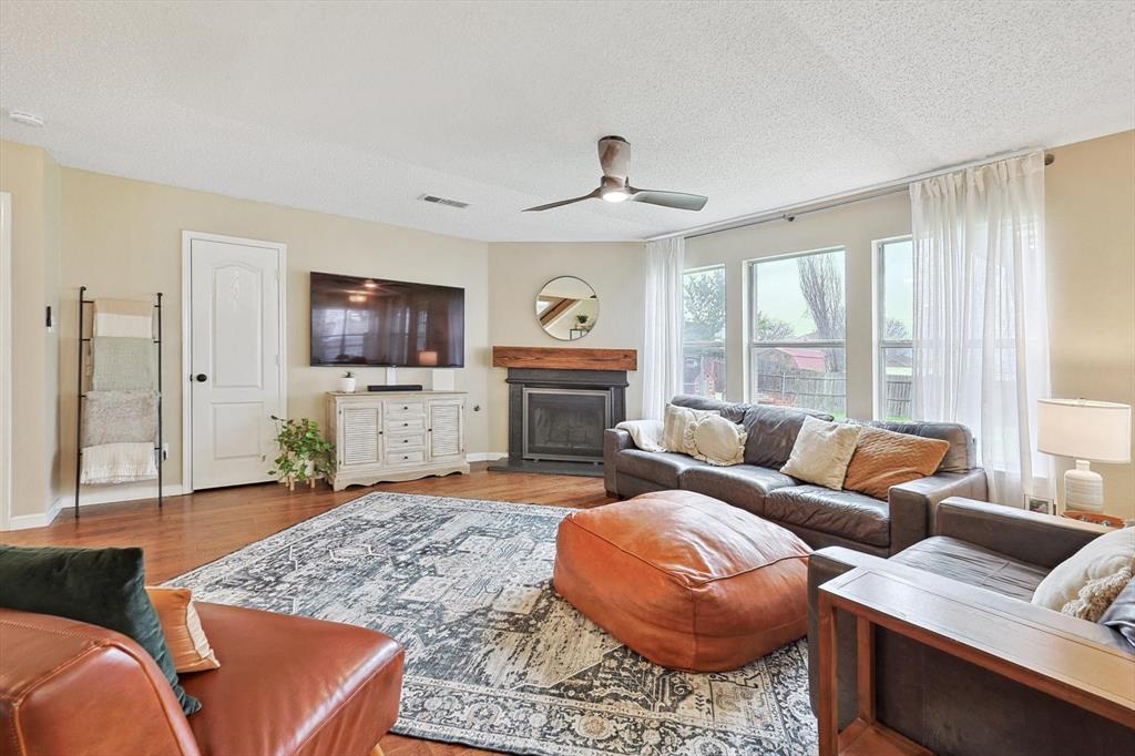 1016 Ridgetop Drive Justin, TX 76247 - Photo 9 of 40 Living room with a fireplace with raised hearth, a textured ceiling, a ceiling fan, and wood finished floors