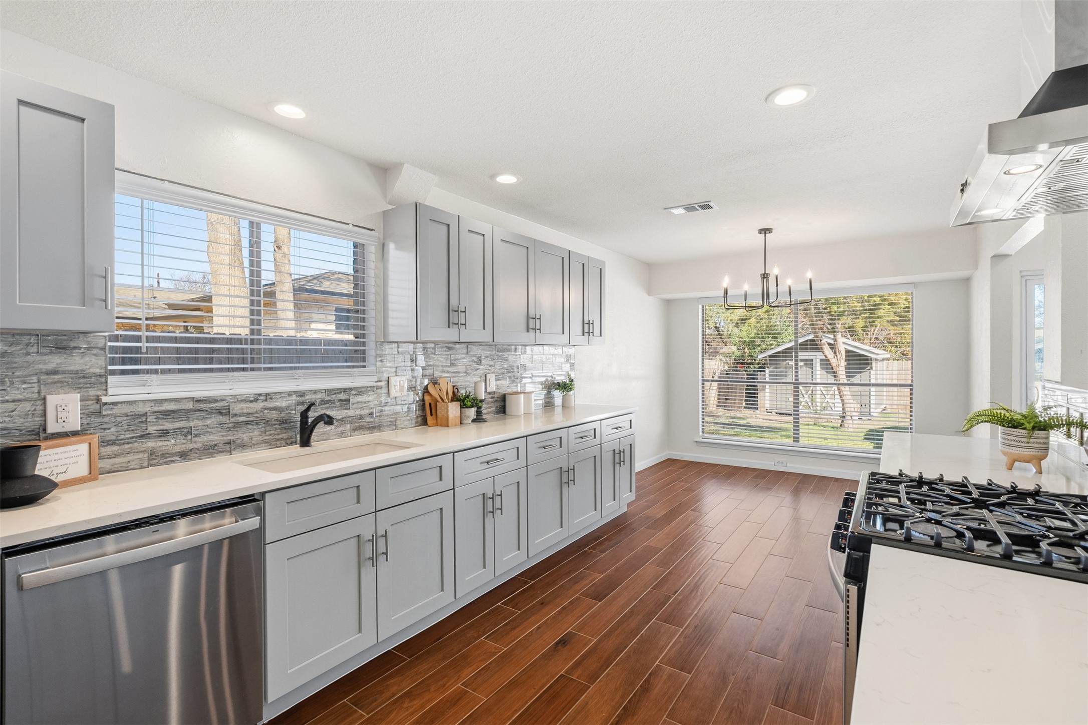 12401 Rusted Nail Cove Austin, TX 78750 - Photo 12 of 34 Kitchen featuring stainless steel dishwasher, wall chimney range hood, tasteful backsplash, pendant lighting, and gas stove