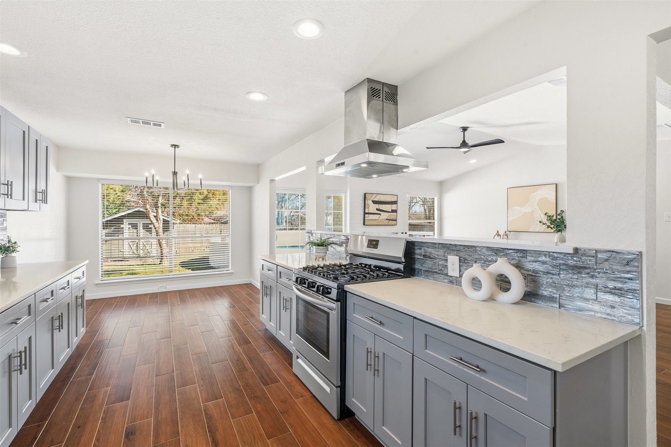12401 Rusted Nail Cove Austin, TX 78750 - Photo 13 of 34 Kitchen with gray cabinetry, stainless steel gas stove, light stone counters, island range hood, and wood tiled floors