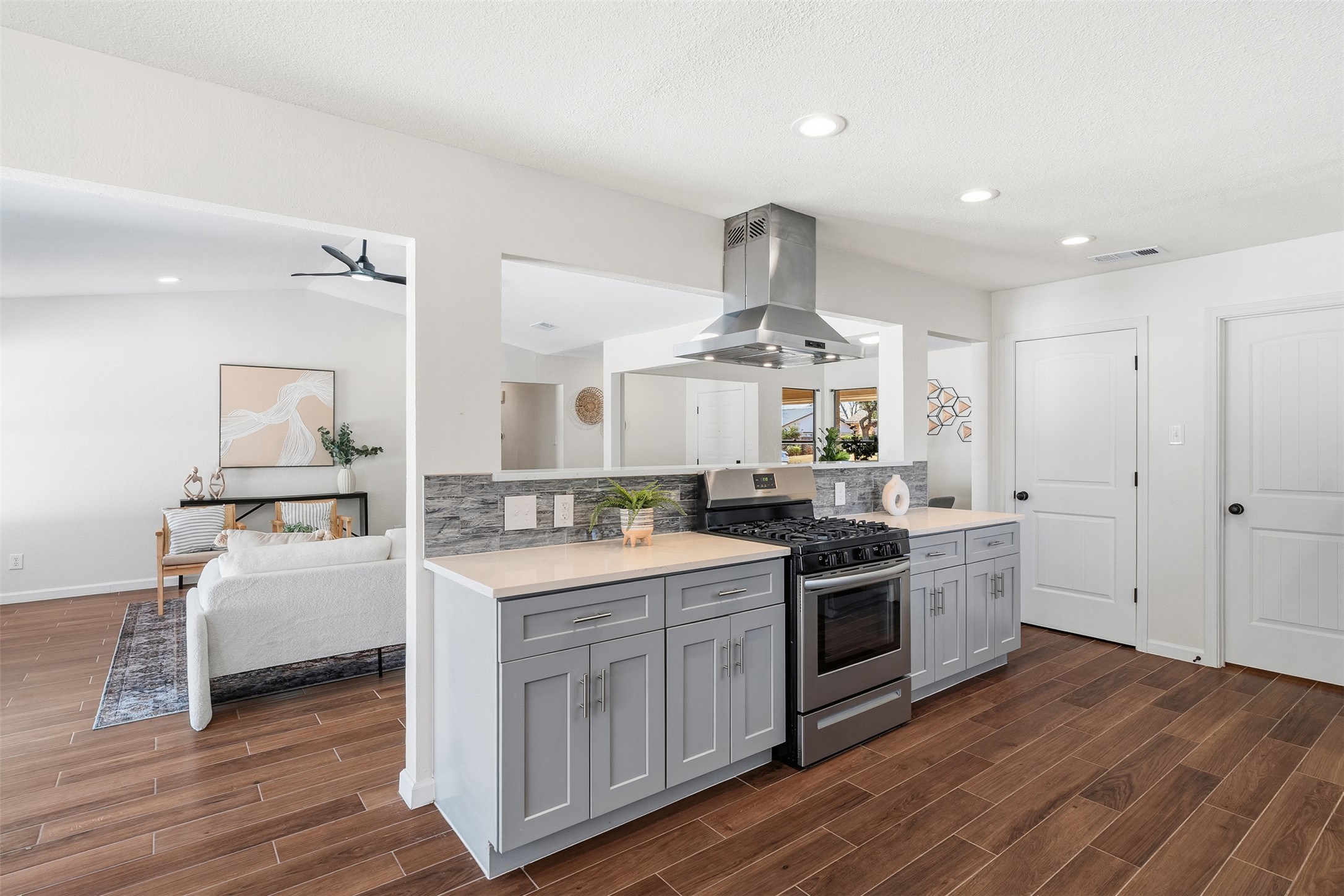 12401 Rusted Nail Cove Austin, TX 78750 - Photo 14 of 34 Kitchen featuring stainless steel range with gas cooktop, gray cabinetry, backsplash, island range hood, and wood finish floors