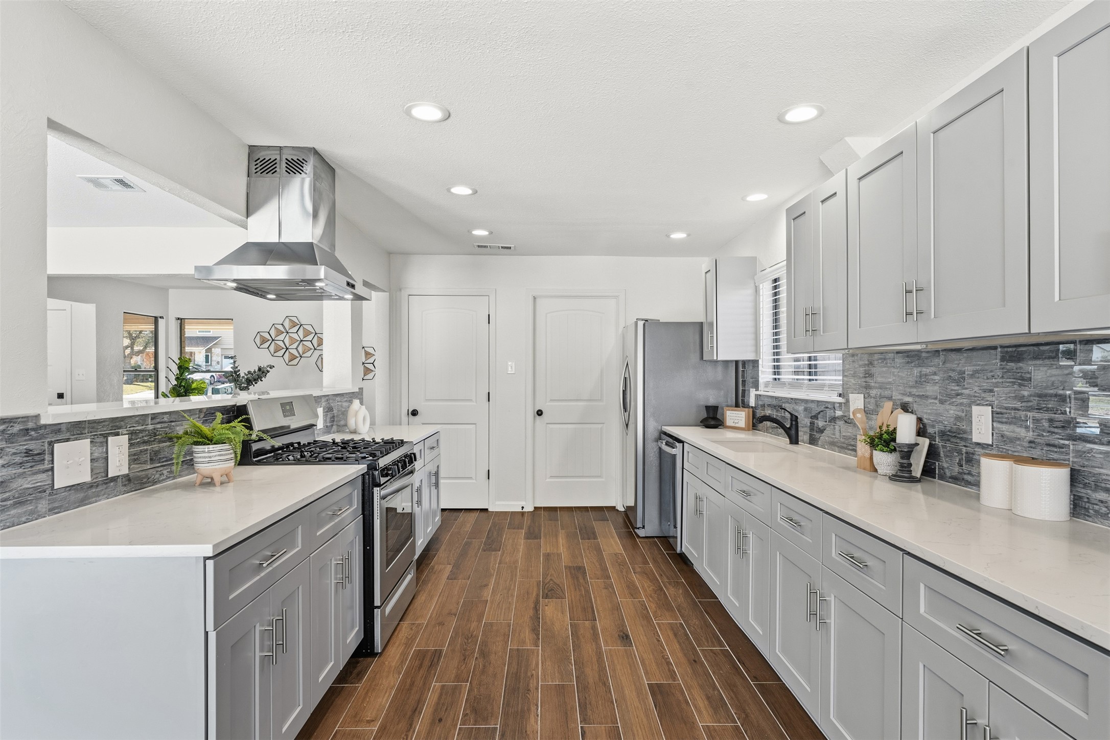 12401 Rusted Nail Cove Austin, TX 78750 - Photo 16 of 34 Kitchen with decorative backsplash, stainless steel appliances, island range hood, gray cabinetry, and wood finish floors