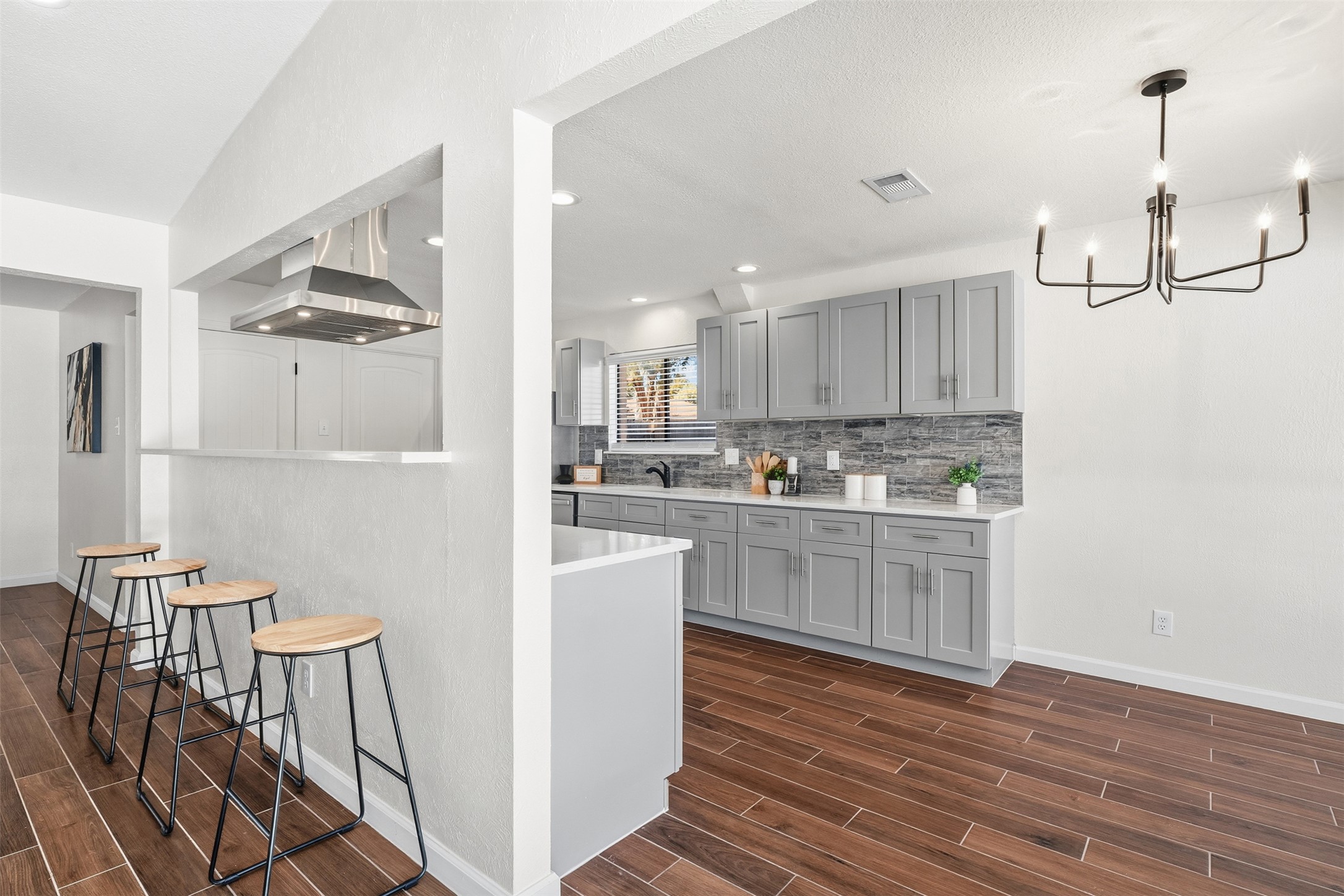 12401 Rusted Nail Cove Austin, TX 78750 - Photo 17 of 34 Kitchen with gray cabinets, wood finish floors, a kitchen breakfast bar, range hood, and pendant lighting